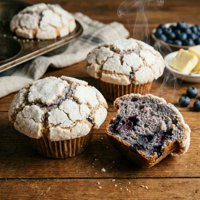 Domed blueberry muffins with a crunchy white sugar crust and soft purple-gray interior with whole bursting blueberries.